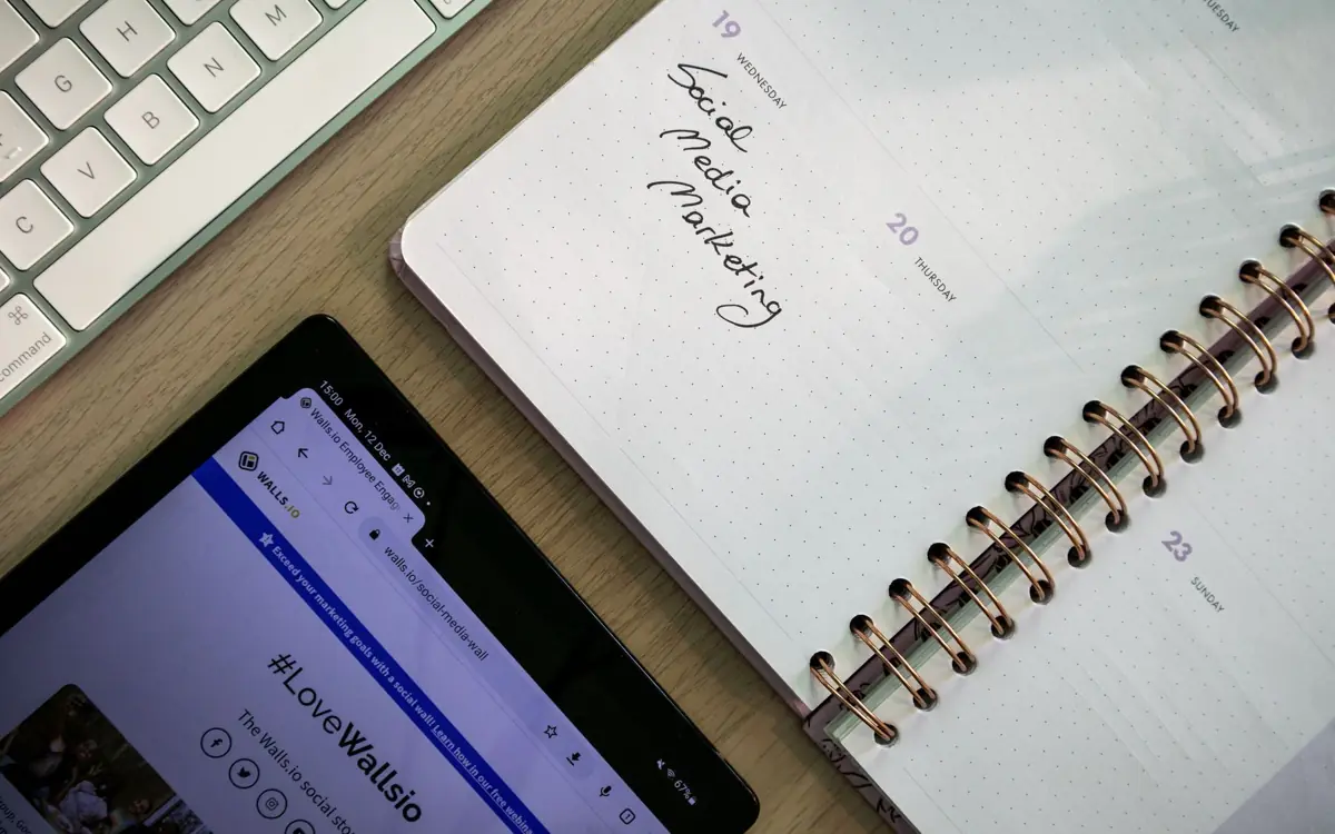 Notebook with a social media marketing plan next to a tablet and keyboard, planning a month of content